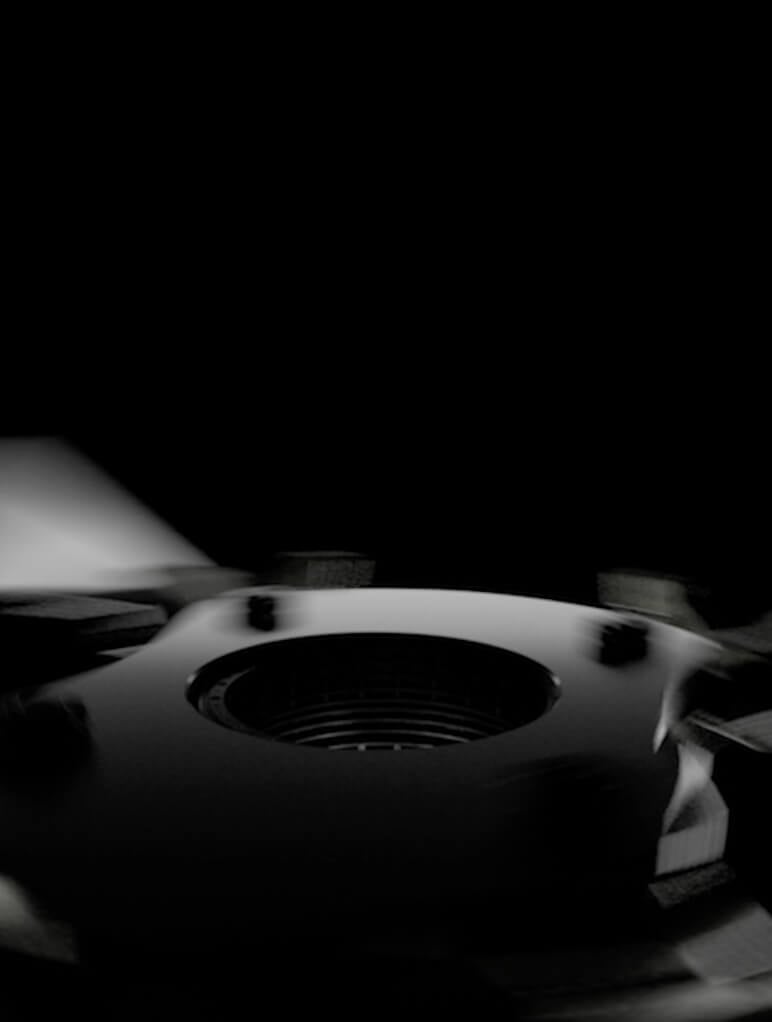 Close-up of a black, shiny circular object with a central hole, set against a dark background. The lighting creates a dramatic contrast, highlighting the object's glossy surface and smooth curves.